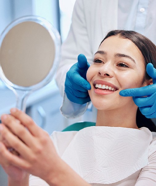 Woman smiling while looking at reflection in handheld mirror