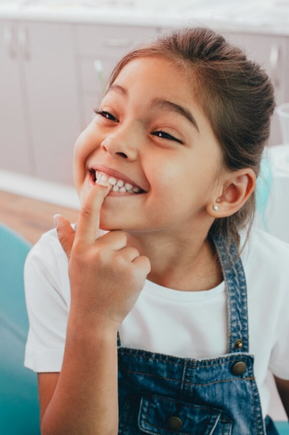 Young girl pointing to smile during children's dentistry visit