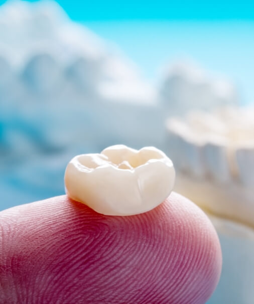 Custom porcelain dental crown on fingertip