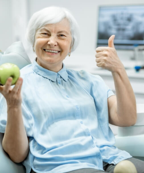 Older woman eating an apple and enjoying the benefits of dental implants