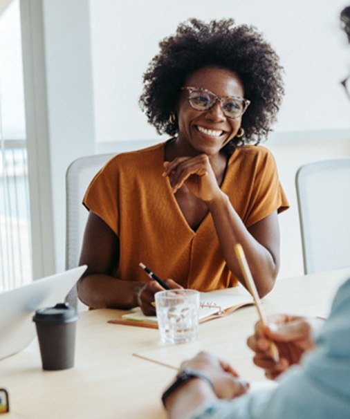 Smiling woman taking notes while talking to colleague