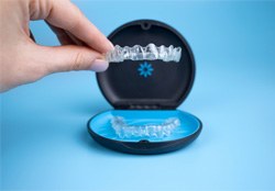 A hand placing Invisalign aligners in a storage case