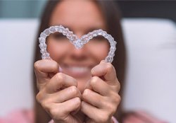 A woman holding Invisalign aligners in the shape of a heart