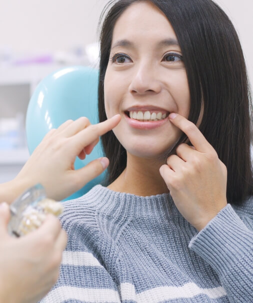 Woman pointing to smilea after tooth replacement with dental implants