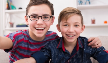 Two teen boys with traditional orthodontics and clear braces smiling