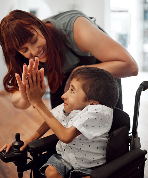 a child in a wheelchair high-fiving his mom