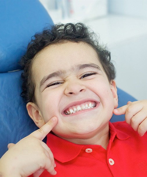 a child smiling and pointing at his teeth