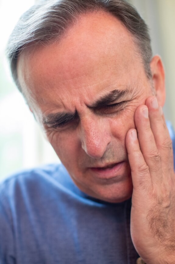 Man with jaw pain before T M J therapy holding his cheek