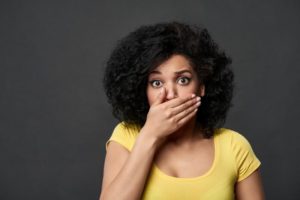 Embarrassed woman covering her mouth after making common teeth whitening mistakes