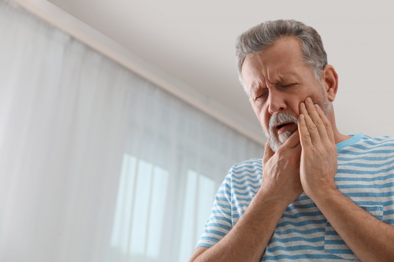 an older gentleman inside his home and holding his cheek in immense pain