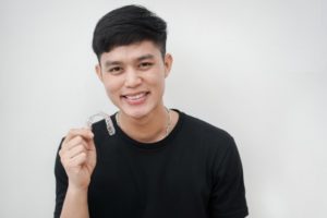 young man in black shirt holding Invisalign aligner 